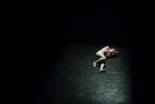 Distraught woman covering her face while lying on the ground against a black background.