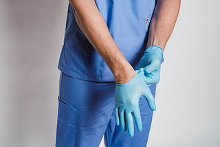 Close up of the hands of a man in blue scrubs pulling on surgical gloves