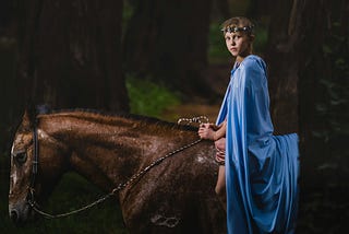 Boy sitting on brown horse beside wearing blue cloak