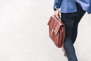 A man walking and carrying a brown leather suitcase for work