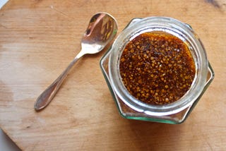 A photo taken from above of a dark, maple-y glass jar of mustard with visible mustard seeds and a small spoon resting nearby