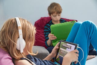 Two young children play the open world game Minecraft on their iPads.