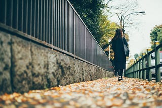 Woman walking down a leaf-strewn path.