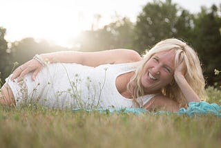 Liz Porter laying on her side in the grass in a white sleeveless dress laughing