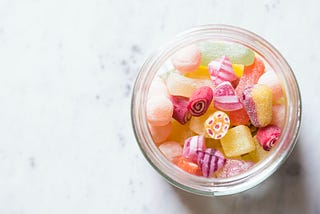 Jar of colourful gummy candies on a white marble background.