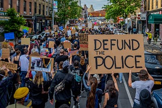 A photo of a protest. One big sign reads “DEFUND THE POLICE.”