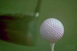 A golf ball on a tee, being hit by a golf club