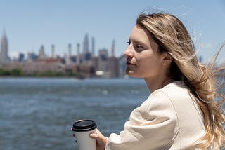 In a possible break, a woman dressed casually sips a coffee. She remains focused on her thoughts, allowing the breeze to blow over her.
