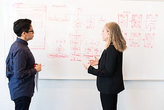 A man and a woman discuss a diagram on a whiteboard