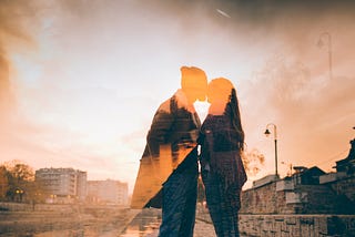 Double exposure orange-filtered photo of a couple kissing against bright sky.