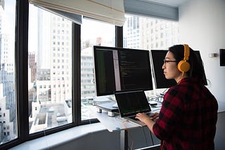 photo of a programmer with multiple screens looking out of an apartment window