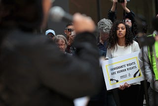 Focus is on a woman holding a “immigrant’s rights are human rights” sign.