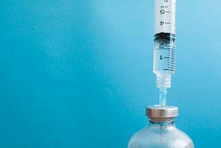 A syringe is injected into a vial against blue background.