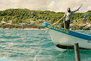 Nipsey Hussle on a boat with his left hand raised. A still from his music video for “Victory Lap”