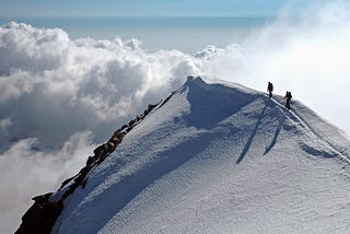 Two people climbing a snow-covered mountain surrounded by clouds