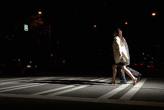Side view of a young man and woman crossing the street at night.