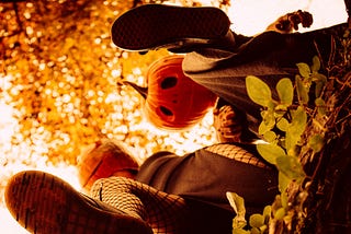 A man and a woman wearing pumpkin masks on Halloween, both have one leg raised kicking something