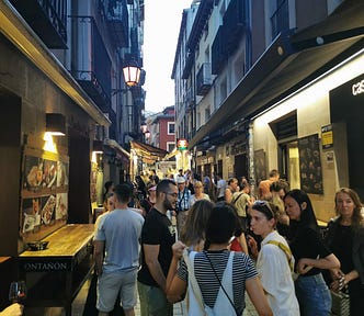 A narrow street filled with people and tapas bars