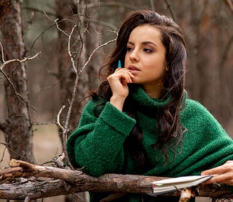 Young dark haired woman in nature, holding a book and pen