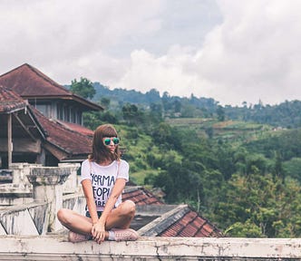 White woman in sunglasses sitting atop a stone wall in Thailand.