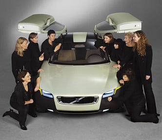 The nine women, all dressed in black, and the greenish, gull-winged YCC car that they designed.