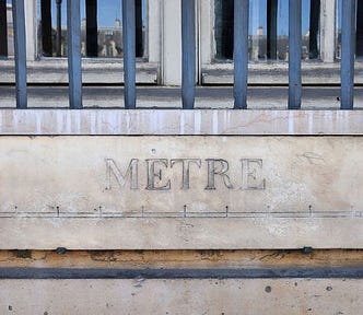 A measurement point in marble on the side of a building in paris, with two metal blocks one meter apart, engraving with 10 decimals between and the word “METRE” carved on top in Didone