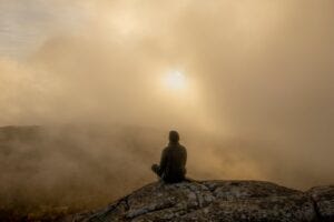 Image of person sat on a mountain in the mist, with the sun trying to break through to illustrate post