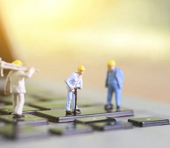 3 figurines of male construction workers wearing yellow hats, standing on a black computer keyboard
