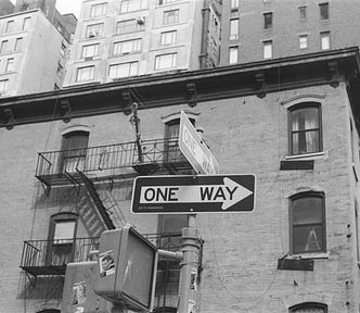 A black-and-white photo of a “one-way sign” in front of a building.