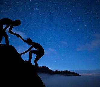 Against a blue background, a silhouetted figure helps another silhouetted figure climb up an incline.