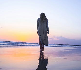 Woman with her back to camera walking on the beach with a beautiful sunset