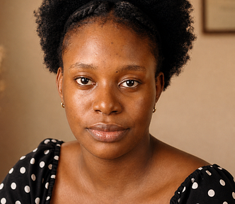 Me, Elma. Natural afro pulled back with a twisted headband, a black and white polka dot top, and the kind of steady eye contact that isn’t asking for anything. Warm light, a framed piece just visible behind me.