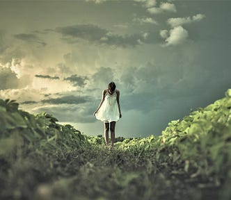 girl in white dress standing in grassy valley with cloudy stormy sky in background