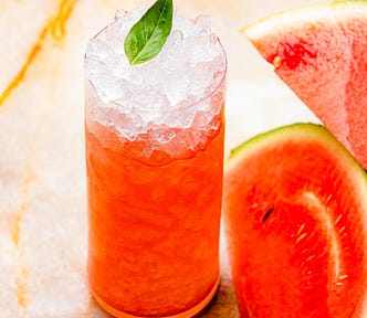 A glass of iced watermelon juice on the counter with cut watermelon next to it.