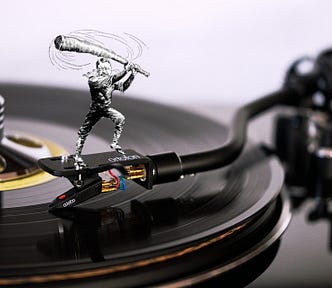 A turntable with a caricature of Teddy Roosevelt as a trustbuster, standing on the tonearm, wielding his ‘big stick.’