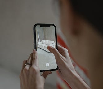 A woman holding a smartphone and viewing a virtual, augmented reality sofa through the phone’s camera.
