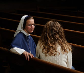A middle-aged nun sitting in a church pew, talking to a young woman
