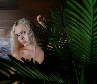 Beautiful blonde, hides behind tropical leaf fronds, peekaboo