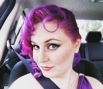 Woman with purple hair sits in car.