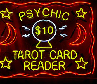 Neon sign reads “Psychic $10 Tarot Card Reader“ with moon and stars graphics and a picture of crystal ball