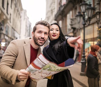 A young man on a city street holds a map and gets directions from a young woman.