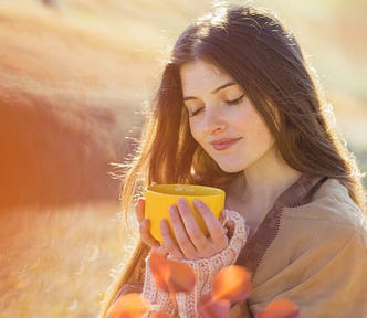Portrait of a pretty young woman on a wheat field as a background. She holds a yellow mug and smiles with her eyes closed. Nutrition and breathing come together.
