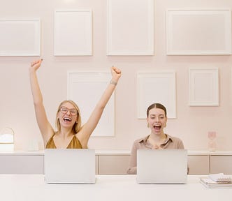 Two Happy Women Sitting in an Office with Blank Frames on a Wall