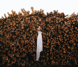 A woman in a long, white dress, apparently floating in mid-air in front of a huge pile of logs.