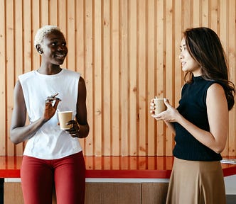 Two women holding paper coffee cups in conversation with one another.