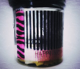 Close up of a plastic jar decorated with washi tape, with the words Happy Notes written on the side.