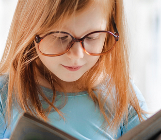 little girl reading a book. She wears glasses.