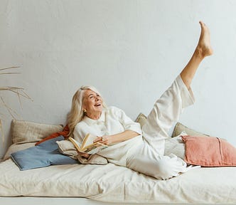 An older, confident, happy woman playfully stretches her leg and laughs.