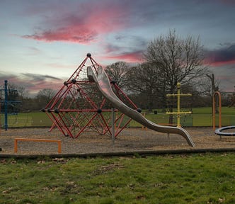 An empty metal playground slide at sunset — tougher days, simpler times.
