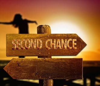 Photo that reads, Second Chance, on a post with arrows pointing in two different directions. Almost sunset in the background, a woman stands, leaning back a bit, with outstretched arms,  embracing the moment.